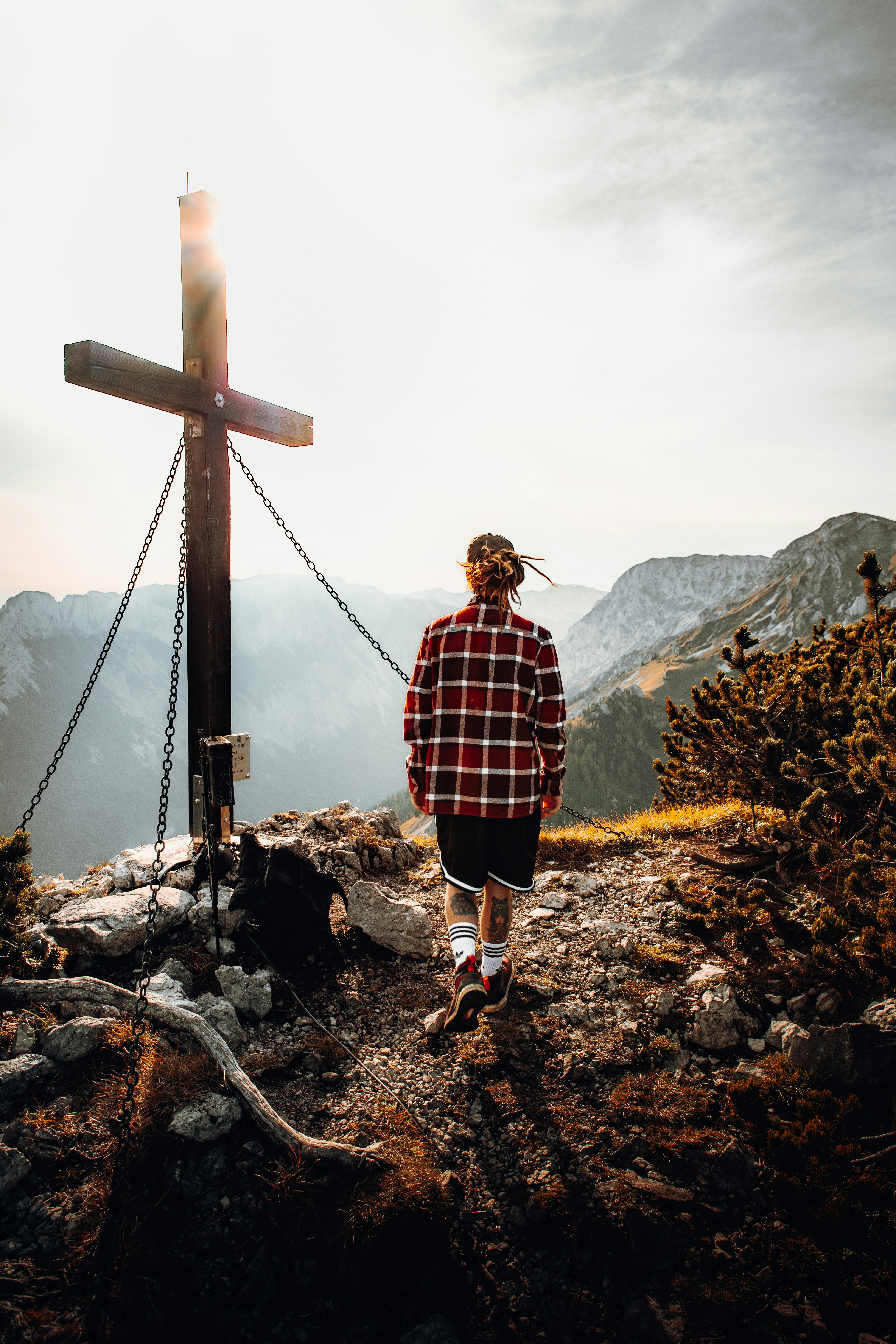 woman in red and black plaid dress shirt standing on brown wooden cross during daytime